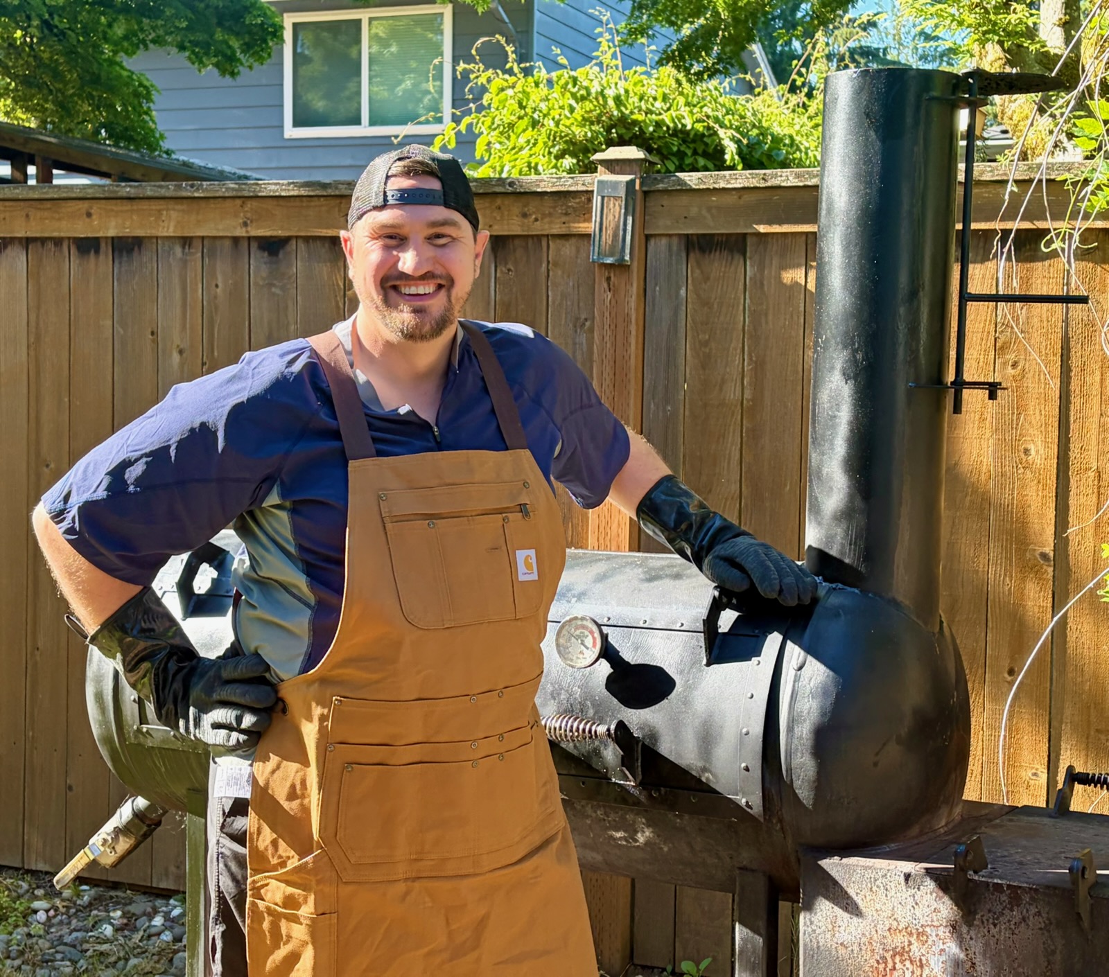 Pitmaster Kristopher Day standing next to a large offset smoker